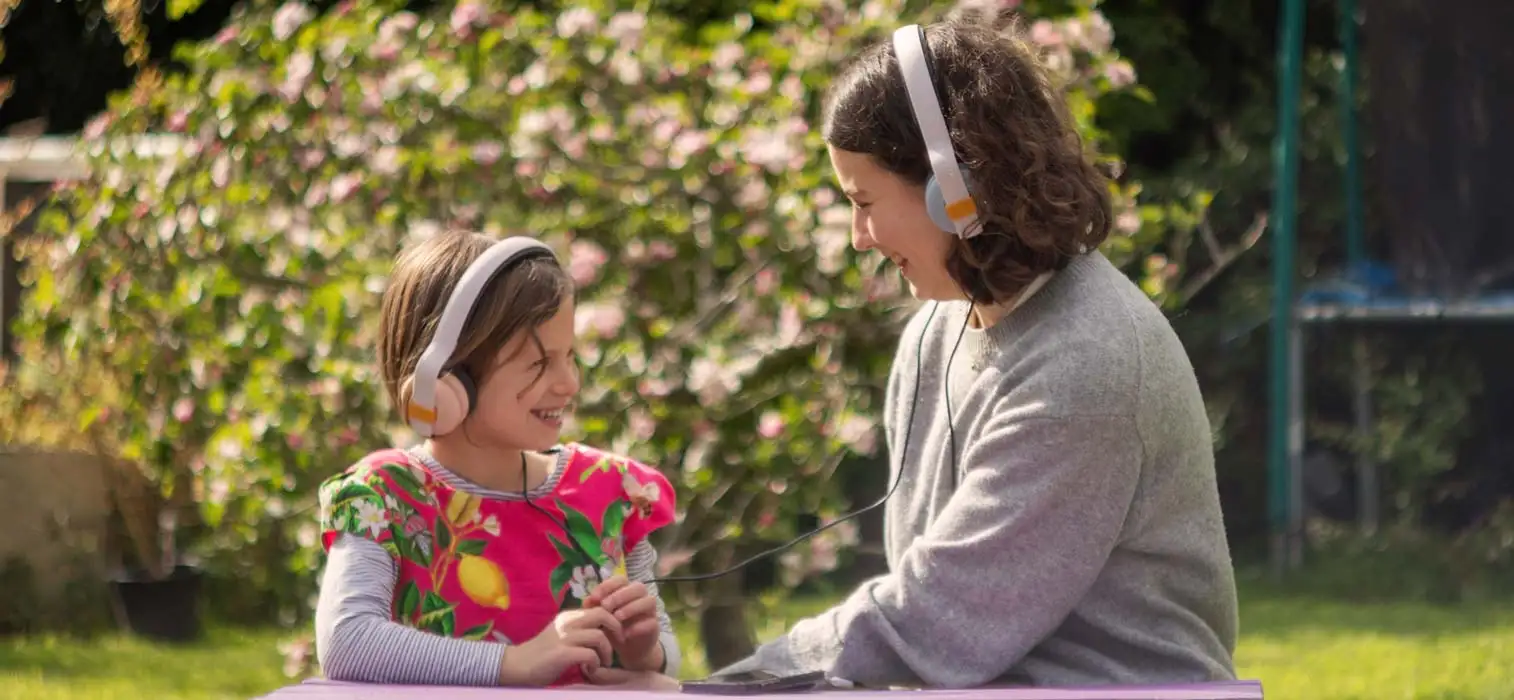 Girl and woman laughing as they listen to music outside on a bench