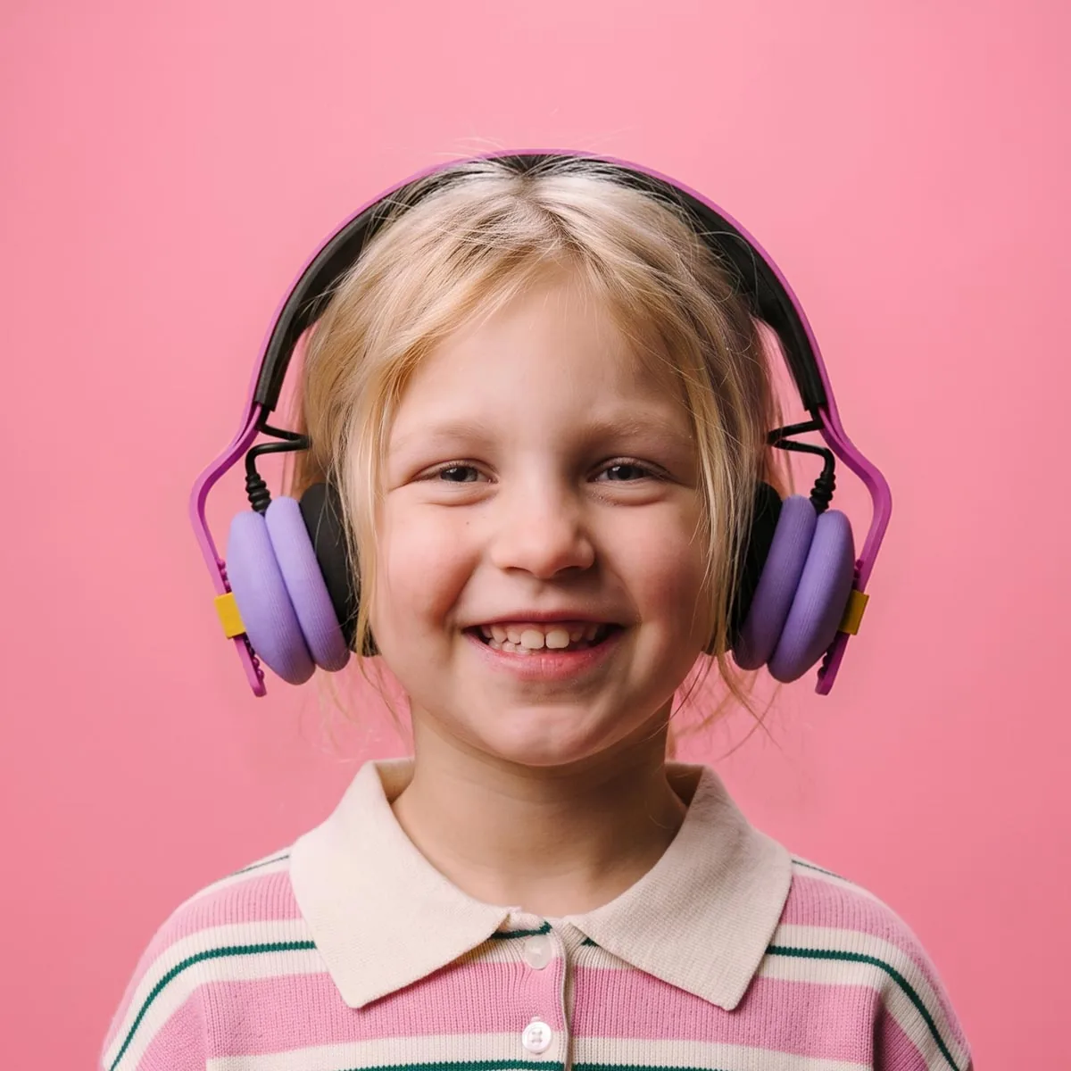 Girl smiling while wearing Kibu Dream Pop headphones with lavender ear cups and a pink headband